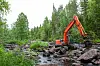 Orange grävmaskin arbetar i en stenig bäckfåra i skog vid Vitån.