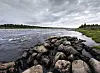 Torne älv vid Kukkolaforsen med stenig strand och molnig himmel.